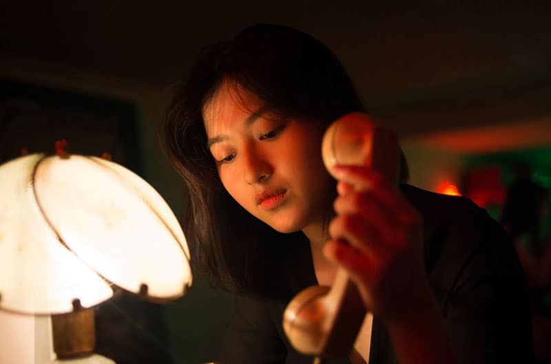 woman holding a telephone in a dark room with only lamp light 