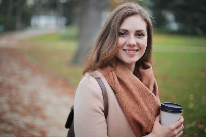 woman holding disposable cup wearing brown winter clothes
