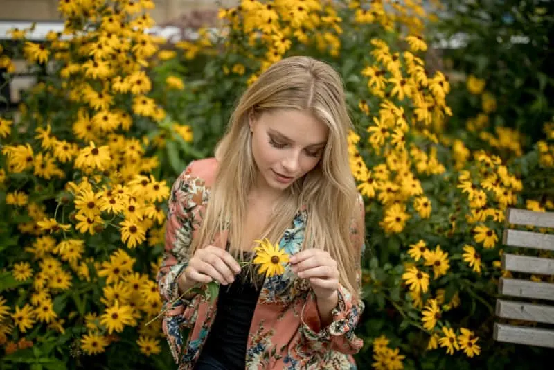 woman in floral jacket holding yellow flower