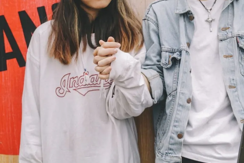 woman in sweatshirt holding man's hand during day