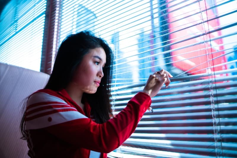 donna con giacca rossa che tiene le tende della finestra durante il giorno