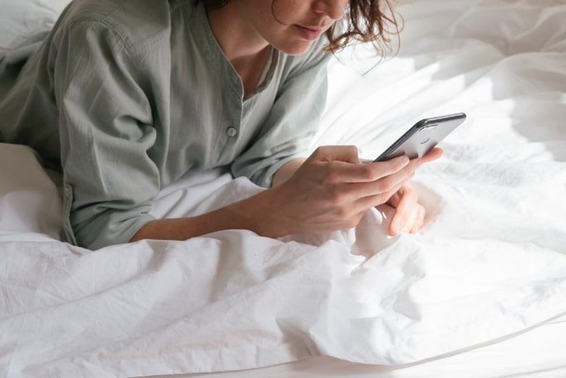 woman lying on bed and using smartphone