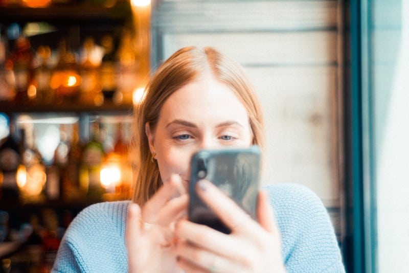 woman in blue sweater looking at smartphone