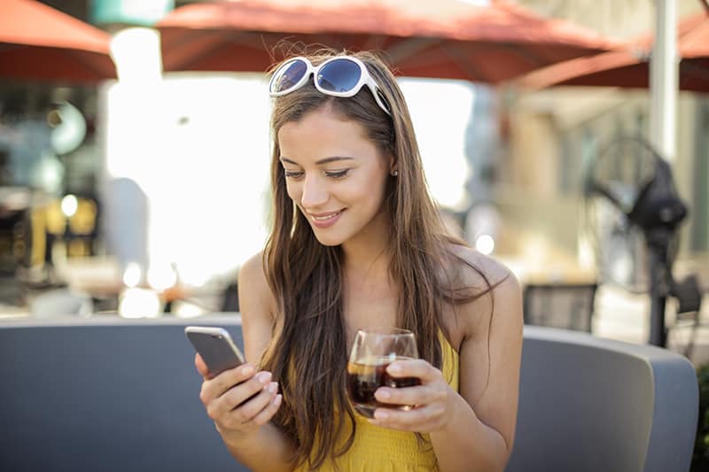 donna che tiene in mano smartphone e bicchiere mentre è seduta all'aperto
