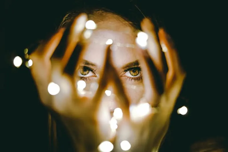 woman holding string lights in front of her eyes