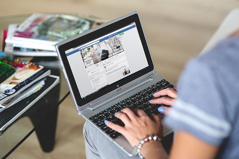 mujer sosteniendo el portatil sobre las rodillas y tecleando en el facebook