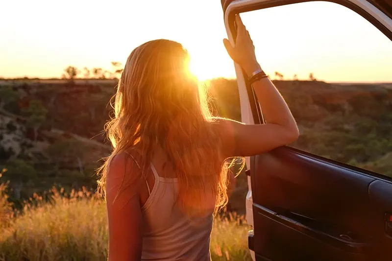 woman holding vehicle door and watching sunset