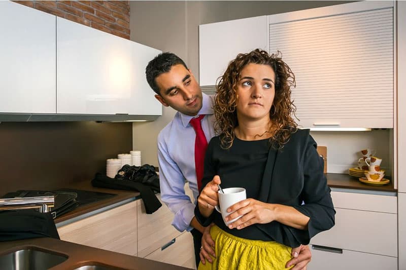 mujer sosteniendo una taza blanca y un hombre detrás de ella sosteniendo sus caderas