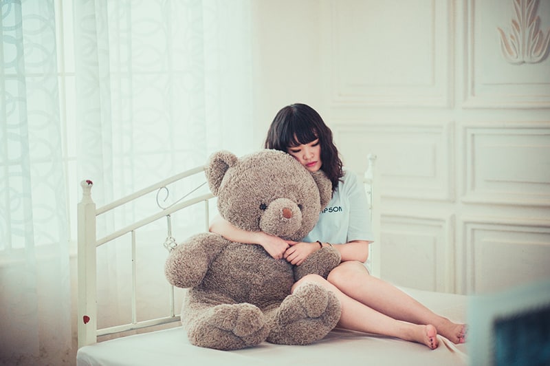 woman hugging grey bear while sitting on the bed