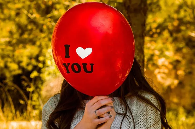 Woman covering face with I Love You Balloon