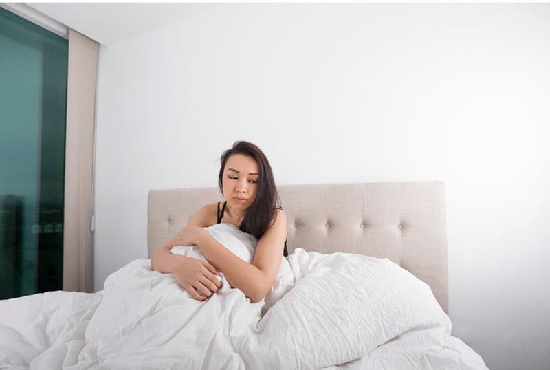 woman in bed alone looking sad covered with white linen