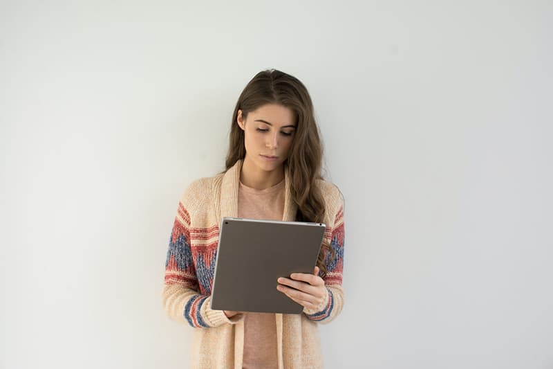 donna con maglione beige che tiene in mano un computer con tablet argentato
