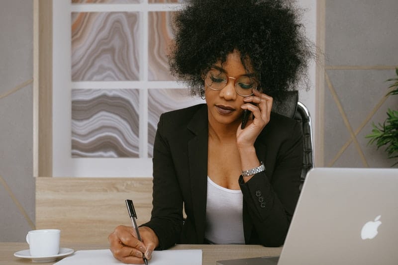 donna in blazer nero che risponde allo smartphone sul tavolo dell'ufficio