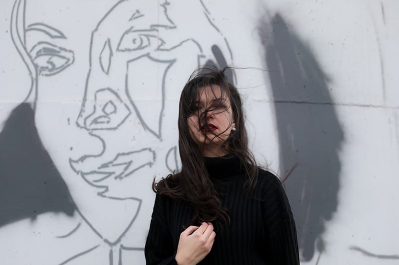 woman in black sweater standing near white wall