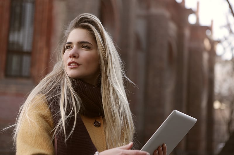 woman in brown coat holding iPad