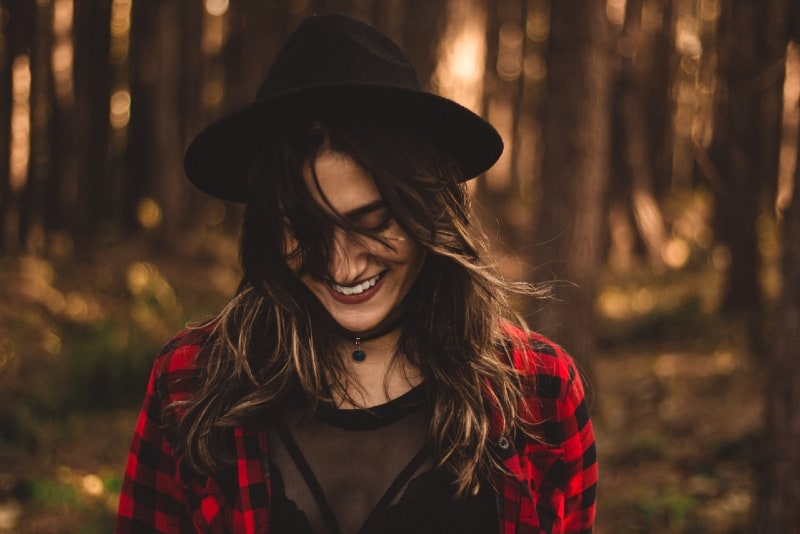 donna sorridente con cappello in piedi nella foresta