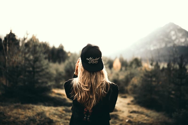 donna bionda con cappello nero in piedi nella foresta