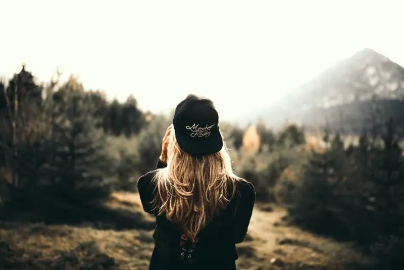 blonde woman with black cap standing in forest