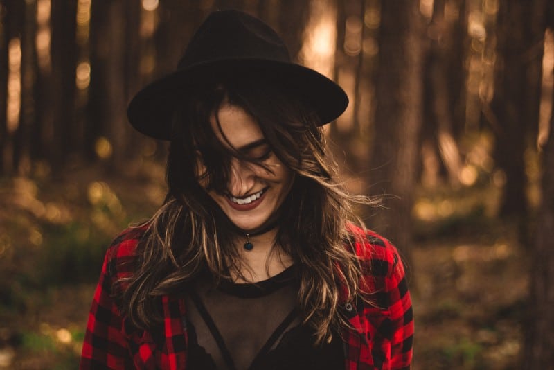 woman with black hat smiling in forest