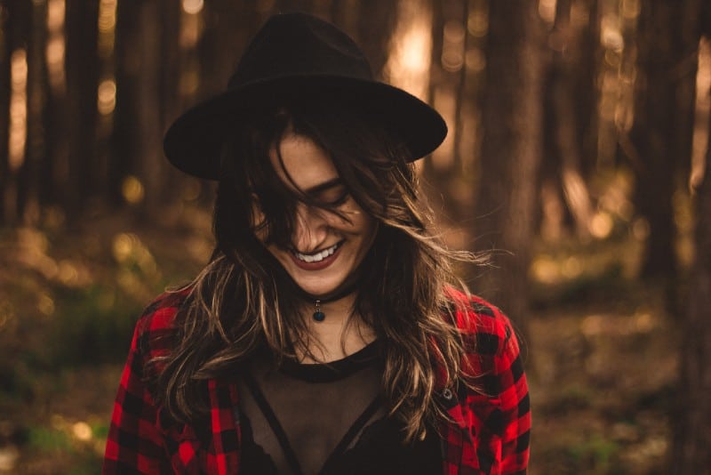 donna con cappello nero che sorride nella foresta