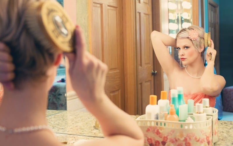 Blonde young woman in front of mirror doing her hair
