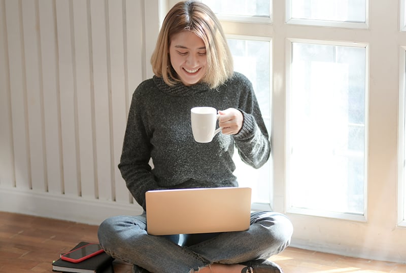 donna con maglione grigio che beve caffè mentre usa il computer portatile