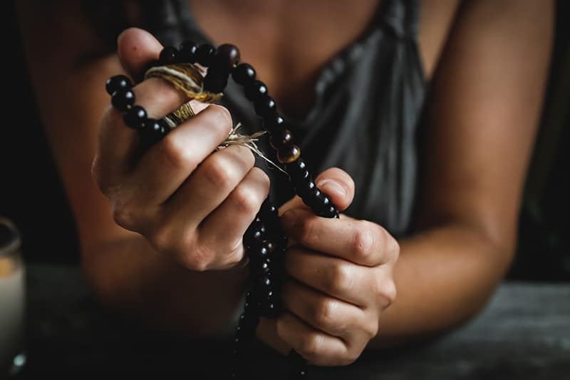 donna con maglietta grigia che tiene in mano un rosario di preghiera