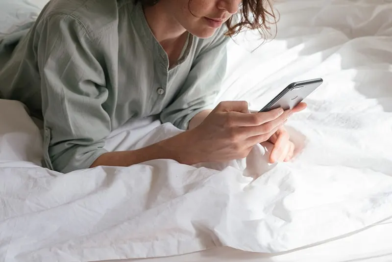woman in grey shirt using smartphone in bed
