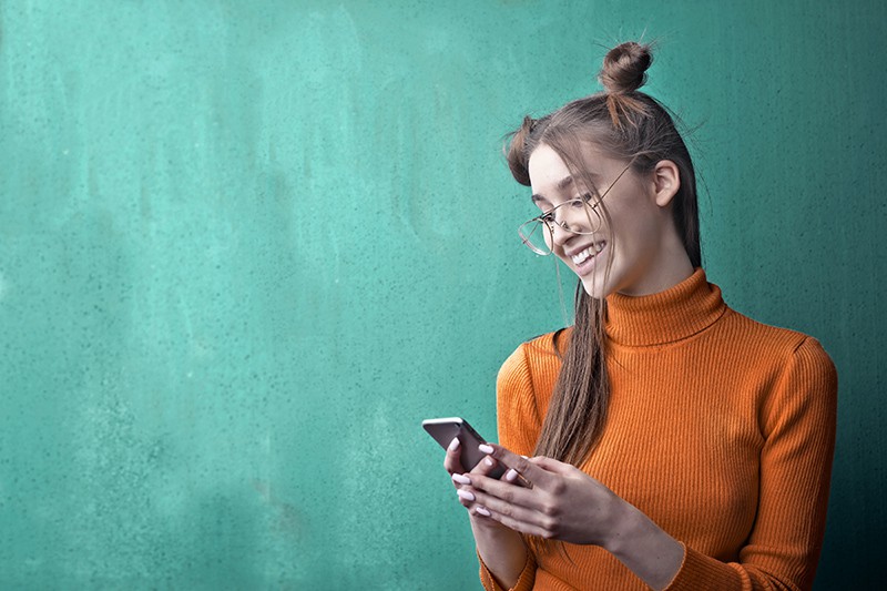 donna con maglione arancione a collo alto che tiene in mano uno smartphone nero