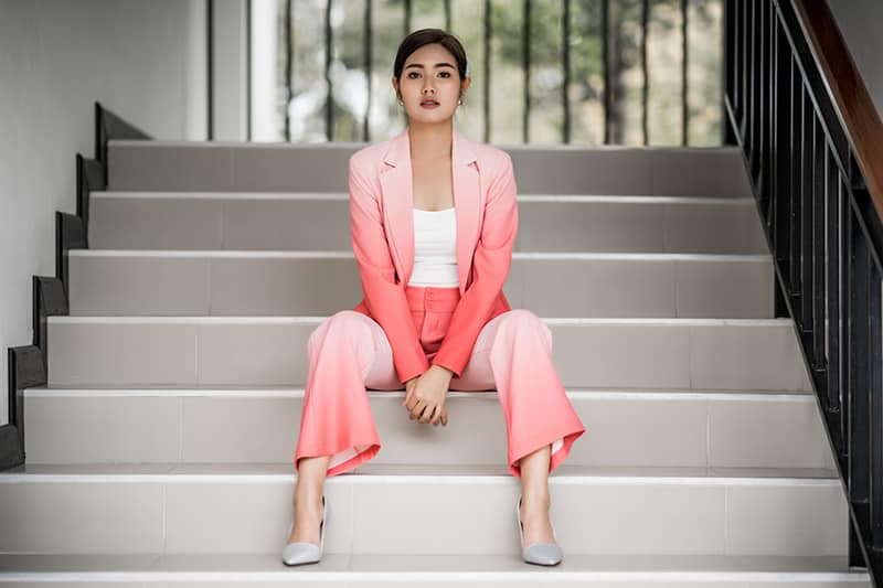 woman in pink blazer and pink pants sitting on white steps 