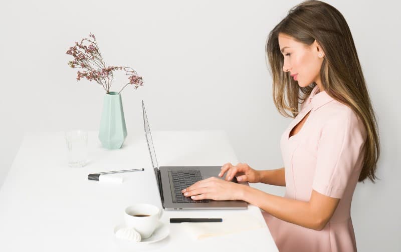 woman in pink dress sitting at a desk using laptop
