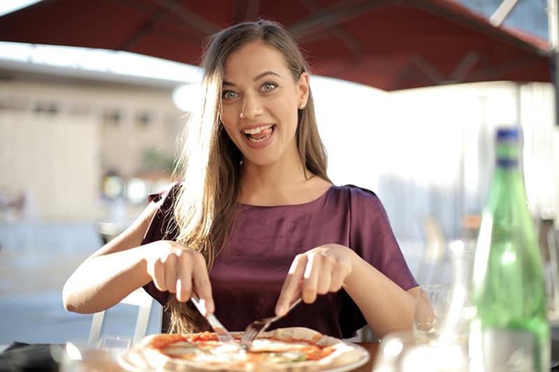 woman in purple top laughing while slicing pizza