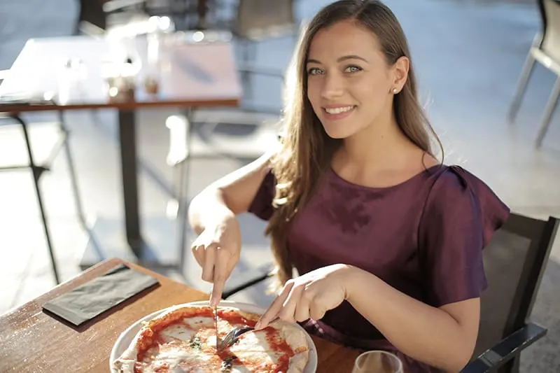 woman in purple top eating pizza