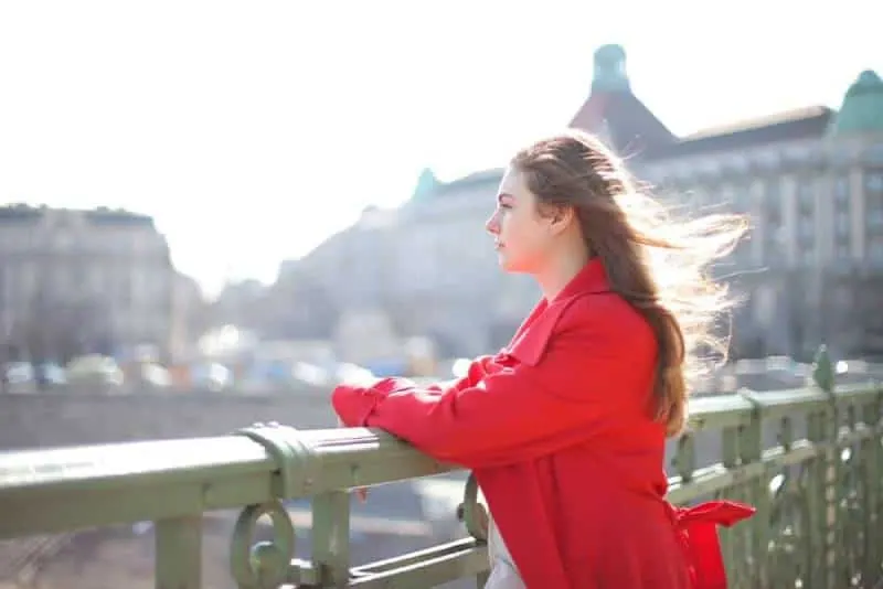 woman in red coat standing near metal railing at the city