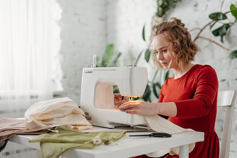 mulher de vestido vermelho a coser, sentada numa cadeira