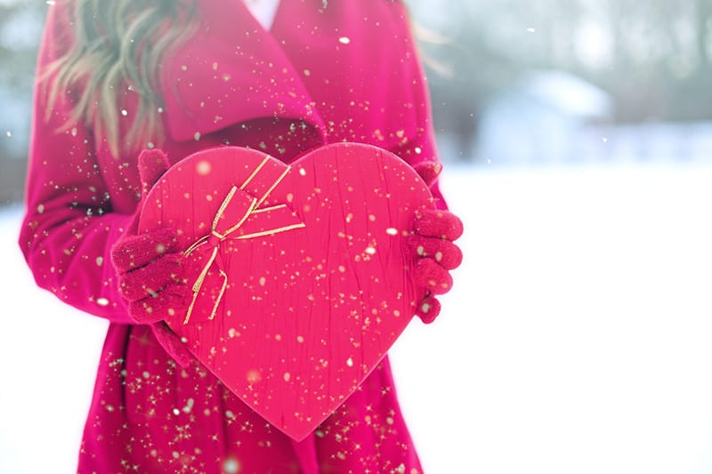 woman in red long sleeved coat holding heart shaped box