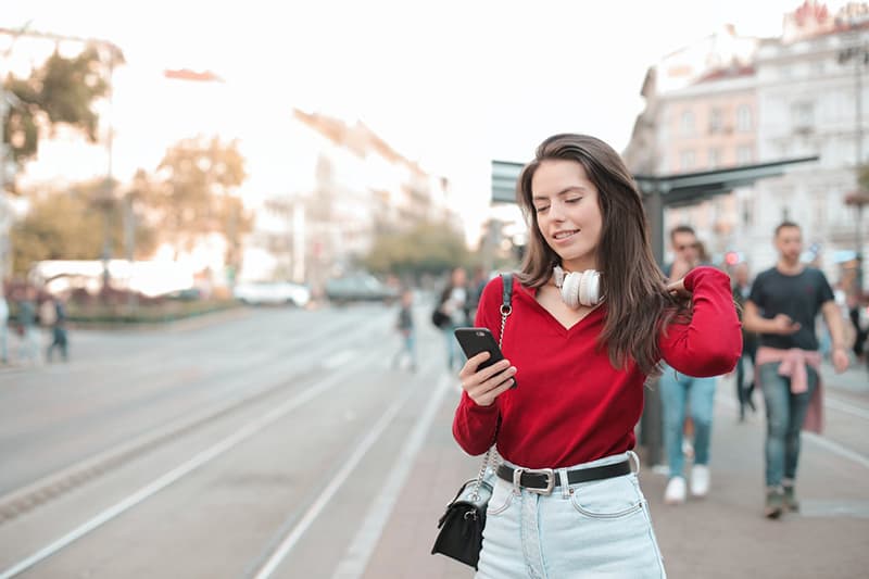 mulher de camisola vermelha a usar o telemóvel enquanto está no passeio