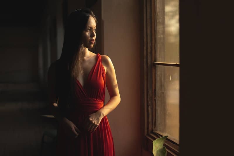 woman in red dress standing and looking out thru the window