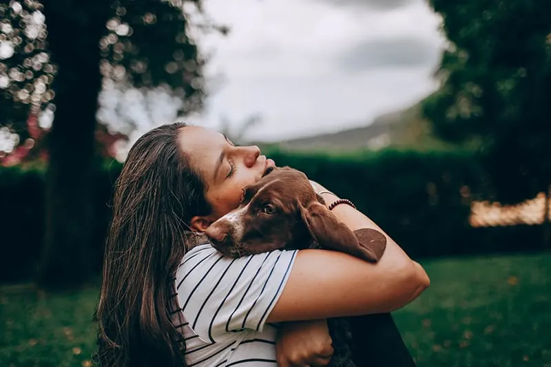 woman in white and black stripe shirt hugging brown dog