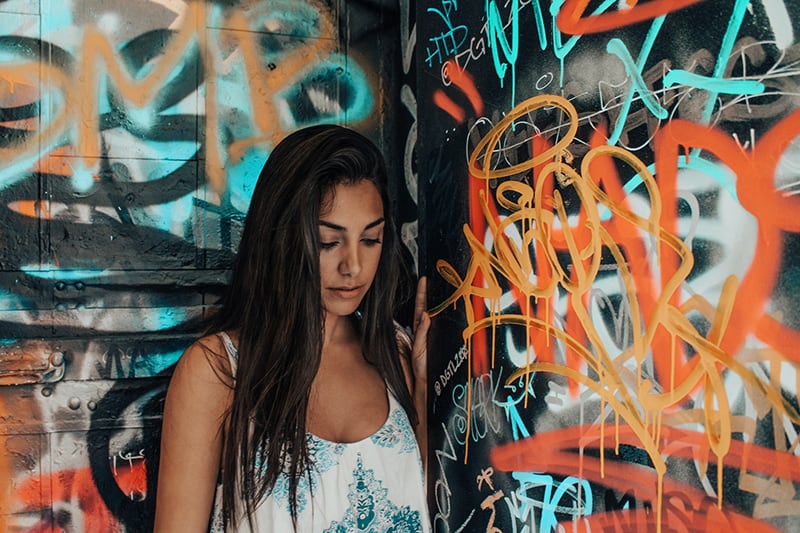 mujer con camiseta de tirantes blanca y azul junto a un muro con graffiti