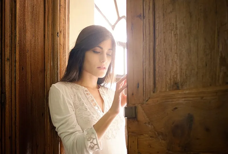 woman in white blouse leaning on brown wooden door frame 