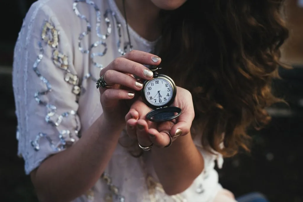 woman in white blouse holding black pocket watch 