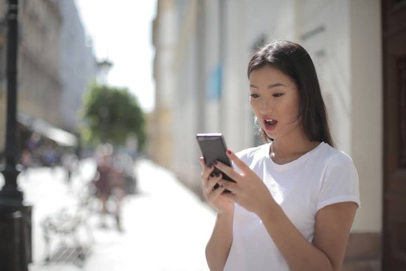 mujer con camiseta blanca de cuello redondo sosteniendo un smartphone negro