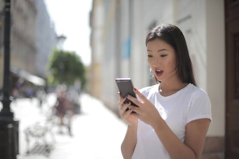 woman in white crew neck t-shirt holding a black smartphone