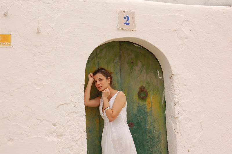 mujer con vestido blanco apoyada en una puerta verde y azul 