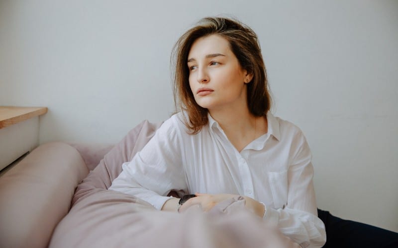 woman in white shirt sitting on a couch looking sad