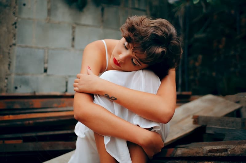 mulher de vestido branco agachada junto a um muro de betão cinzento