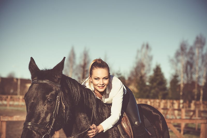 woman in white hoodie riding black horse
