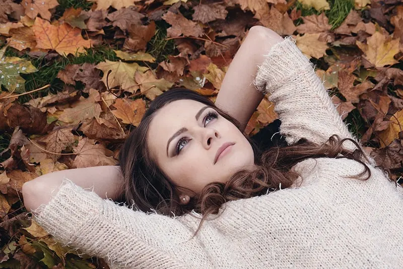 woman in white knit sweater lying on dried leaves