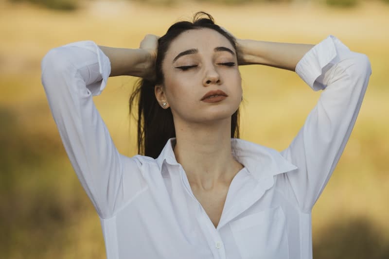 woman in white shirt closing her eyes hands on her head